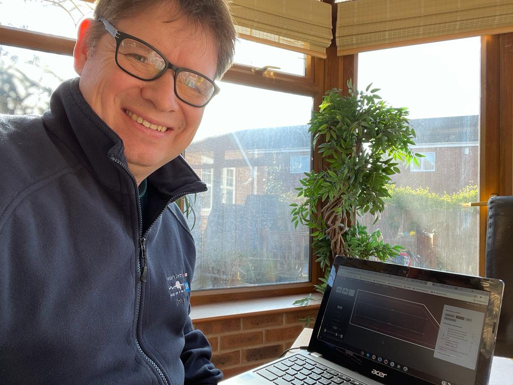 Chris Hector sitting at his home office, a laptop is on a desk with some design work for Solar PV systems.