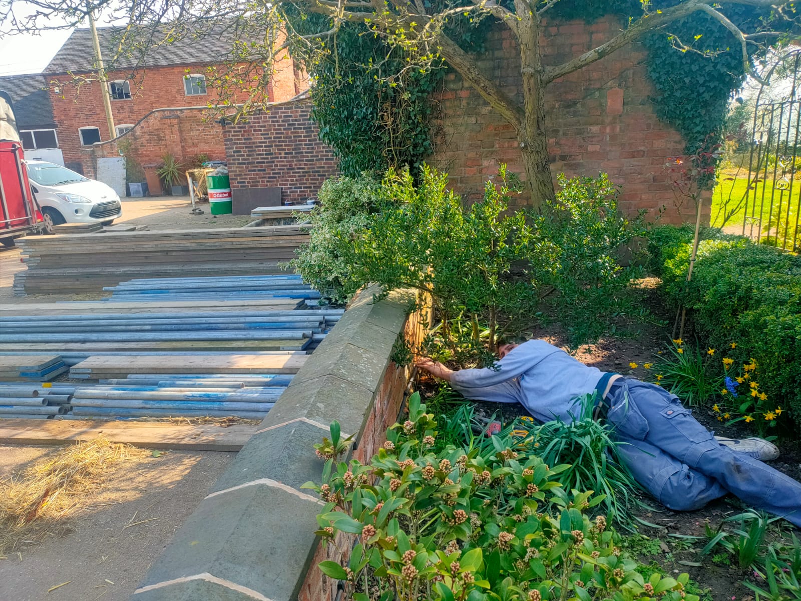 One of our beloved workers Jordan is on the ground covered by grass and other outside items, he is working on a fence or wall and installing the cabling,