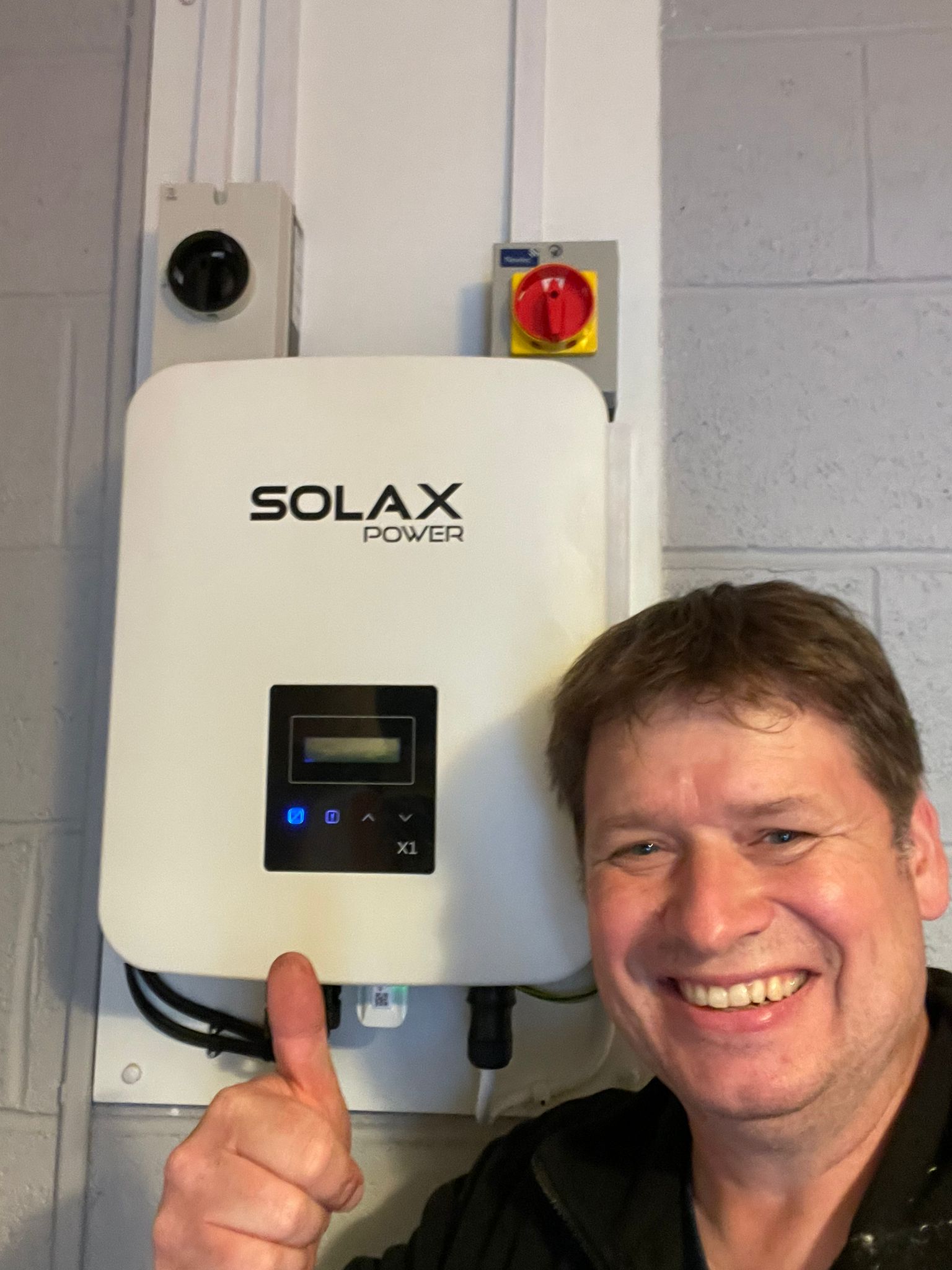 Chris smiling with a thumbs up, behind him is a Solax Power Solax inverter