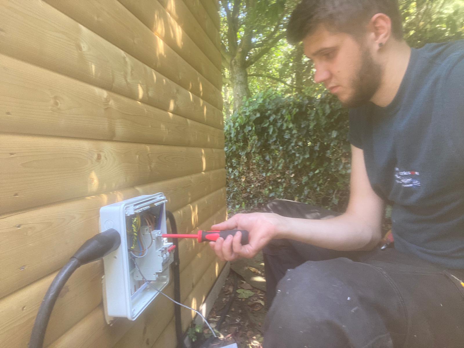 a type of box on a wall in a garden, along with one of our electricians working on it