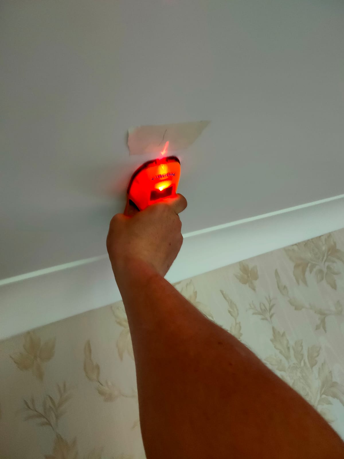 By using a stud finder on the wall we can see where all the beams are, this image is one of our electricians holding a stud finder to the celling.