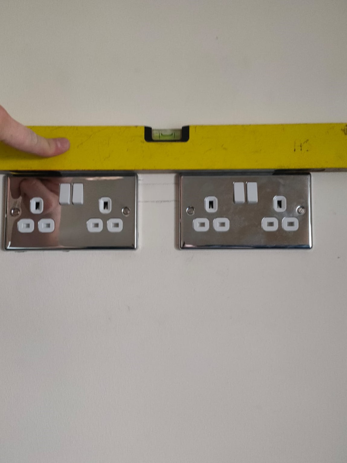 Two sockets on a wall, with one of those straight checker devices, they are aligned perfectly