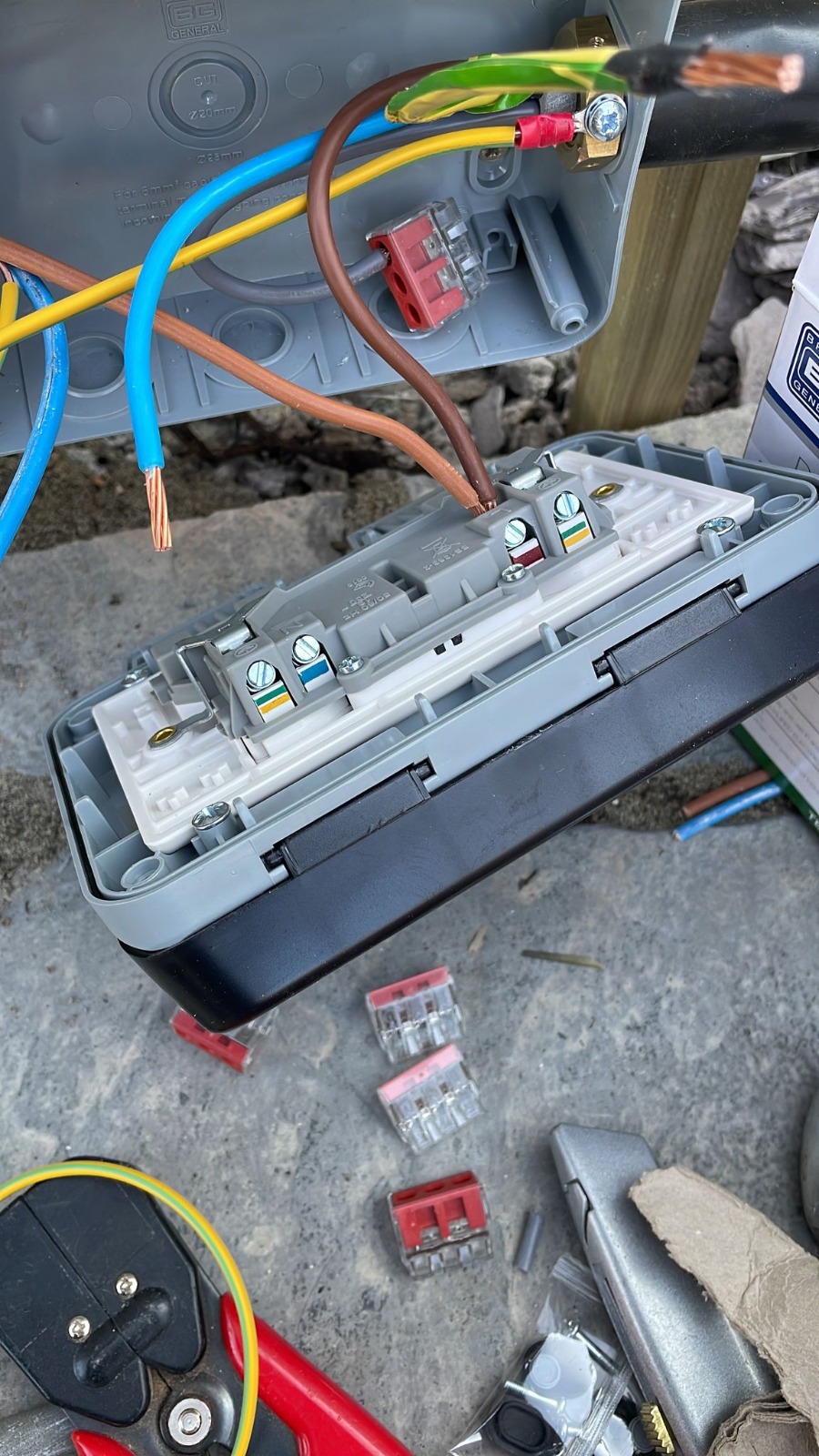This is a weatherproof socket being held by one of our electricians, there is wires and a lot of screws around and they are about to insert another wire in there. 